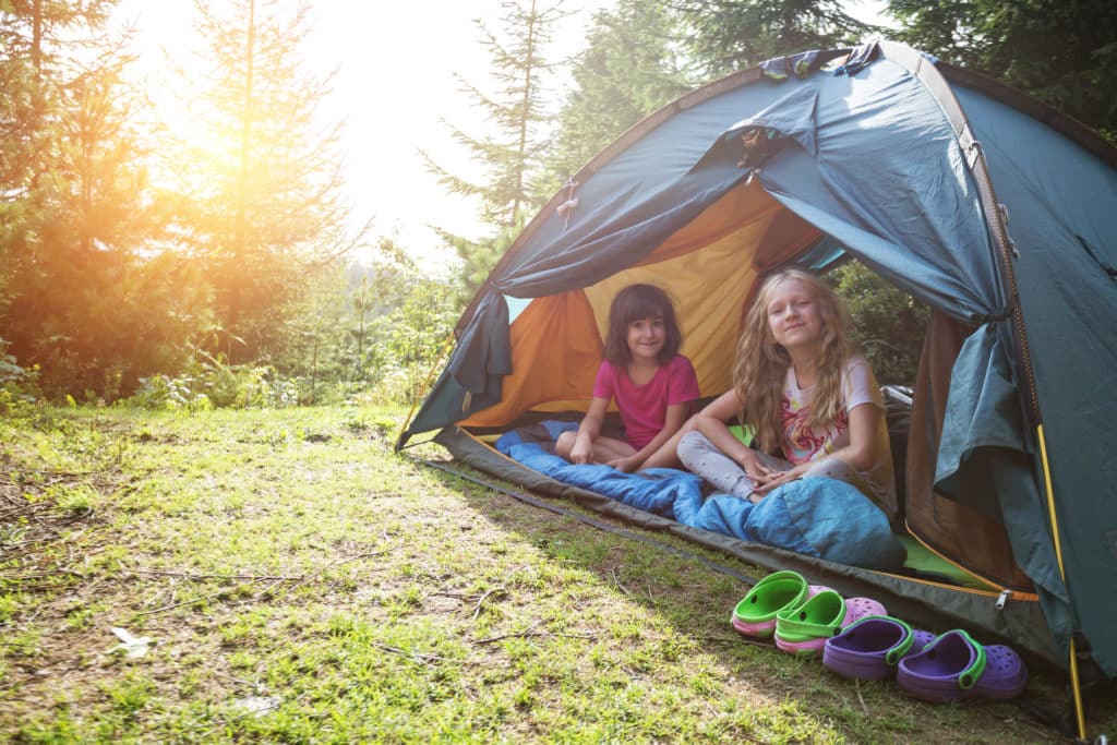Twee meisjes lachend in een tent in de bossen.