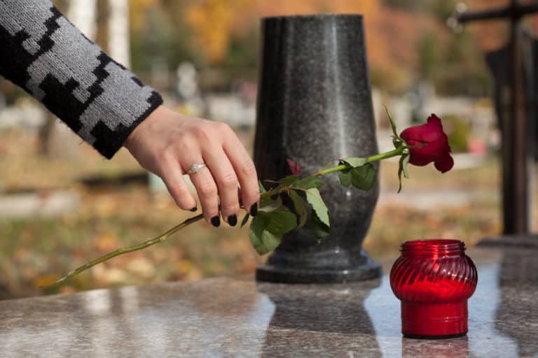 Een vrouw legt een rode roos op een graf.