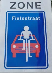 Blauw bord zone fietsstraat: begin van de zone: figuur van witte fietser voor een rode auto
