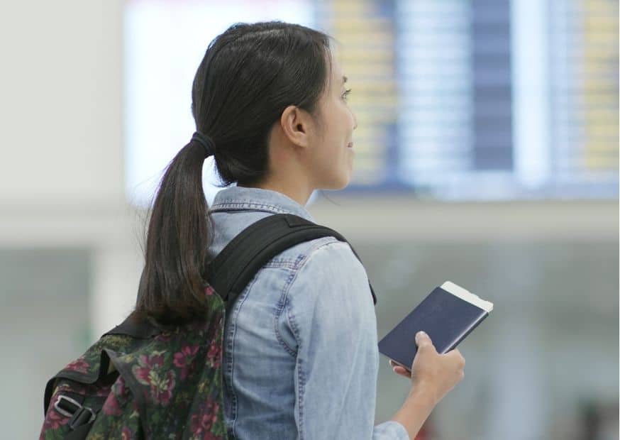 Buitenlandse vrouw met rugzak heeft haar paspoort vast, staat met haar rug schuin naar de camera