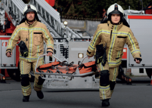 Een brandweerman en brandweervrouw dragen een brancard.
