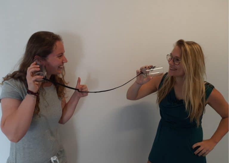 Twee personeelsleden van de communicatiedienst beelden communicatie uit met twee bekers en een touwtje.