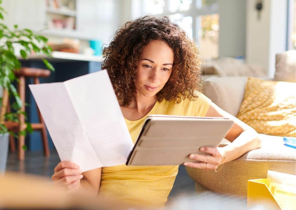 Vrouw die neerzit en een tablet en blad papier bekijkt.
